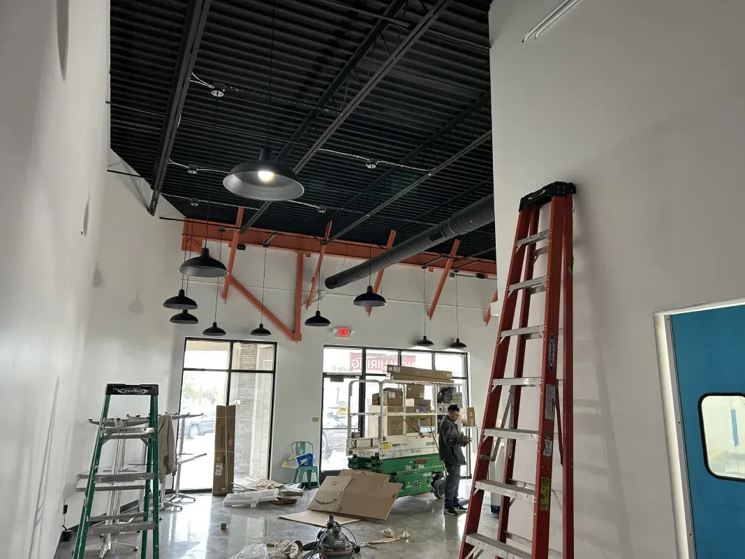 Interior under construction, bare walls, black ceiling, exposed beams, ladder, worker near boxes.