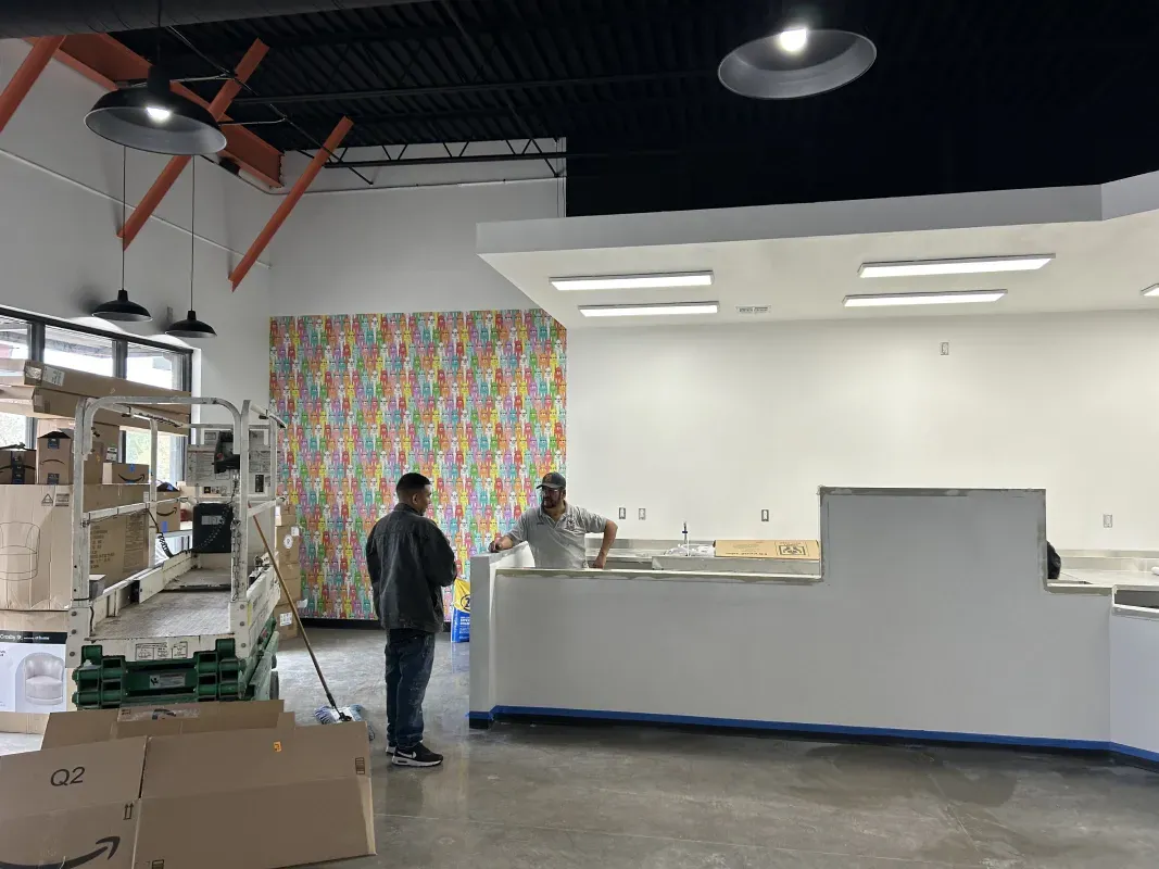 Two men stand in a commercial space under construction near a white counter and a patterned wall.