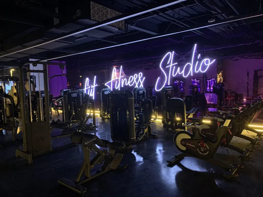 A dimly lit fitness studio with workout equipment and a neon sign that says 