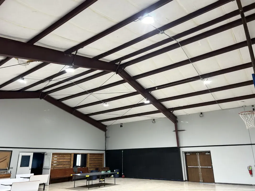 Interior of a gymnasium with brown steel beams, white ceiling, and basketball hoop.