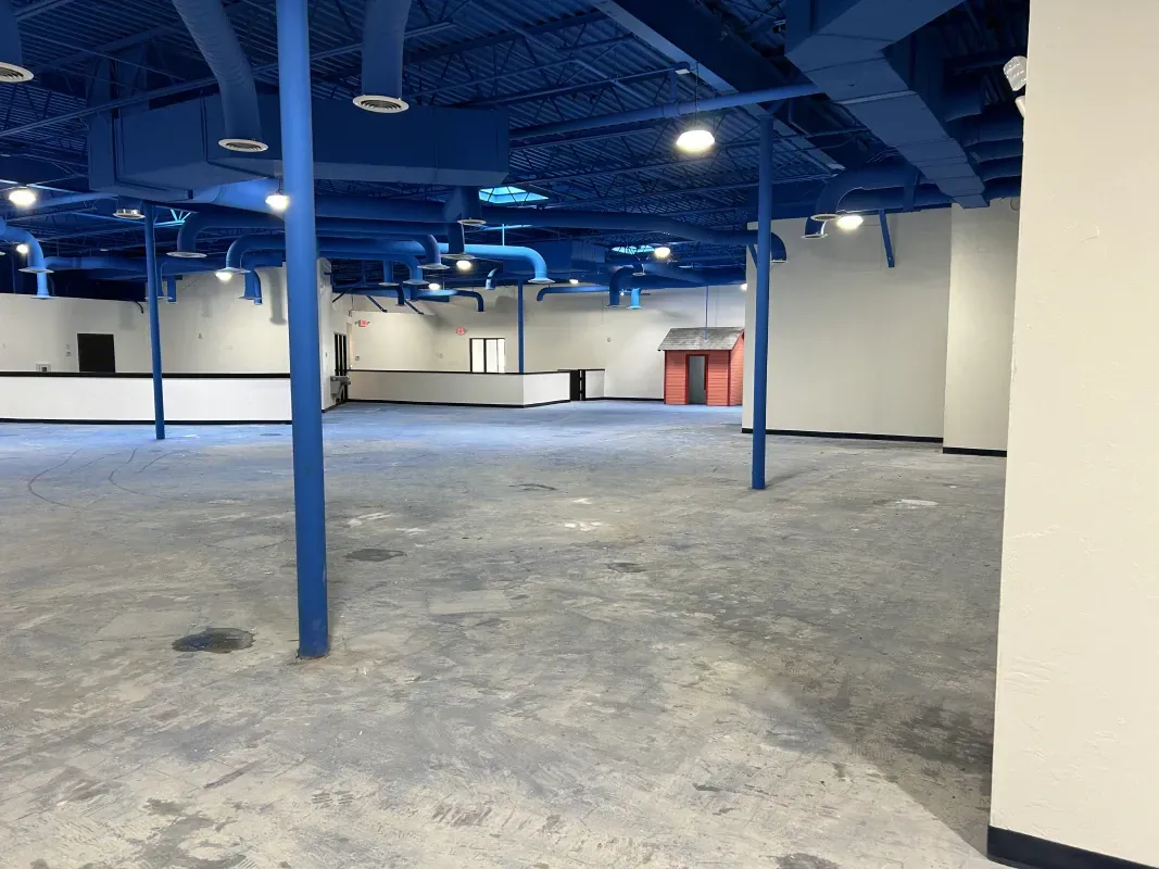 Empty commercial space with blue ceiling and supports; gray floor and white walls.