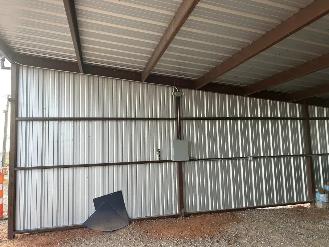 Metal shed interior with corrugated walls, brown beams, and a gravel floor.