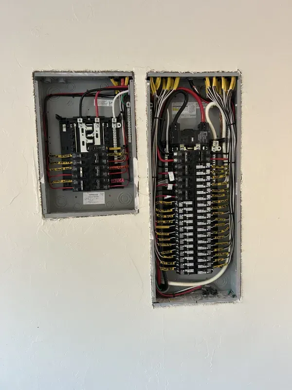 Two electrical panels installed in a wall, showing exposed wires and circuit breakers.
