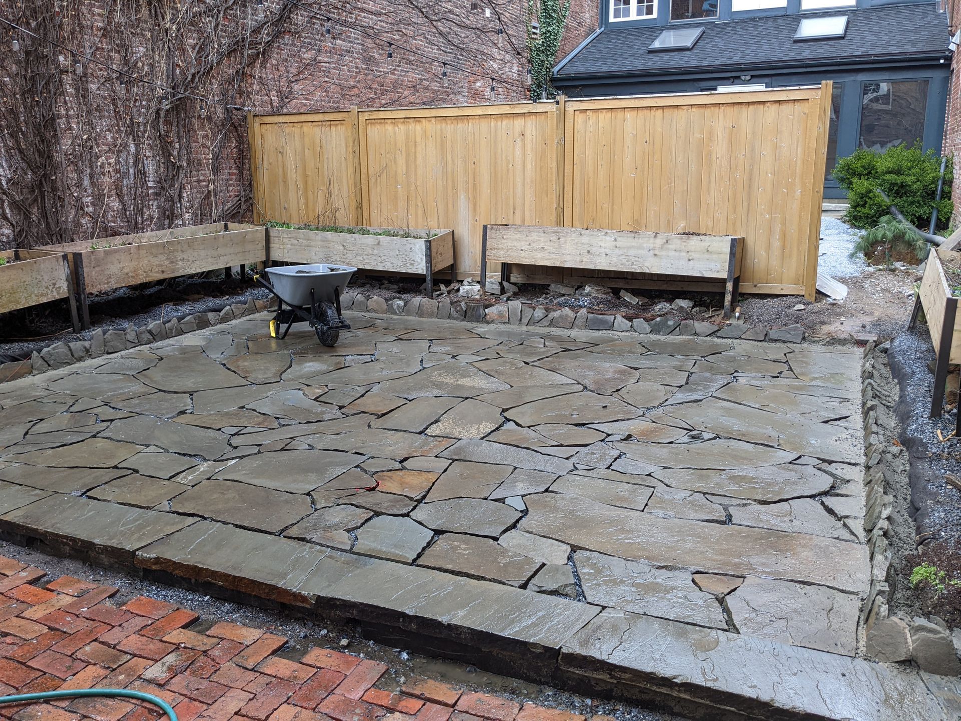 Flagstone patio with wooden planters, wooden fence, and wheelbarrow.