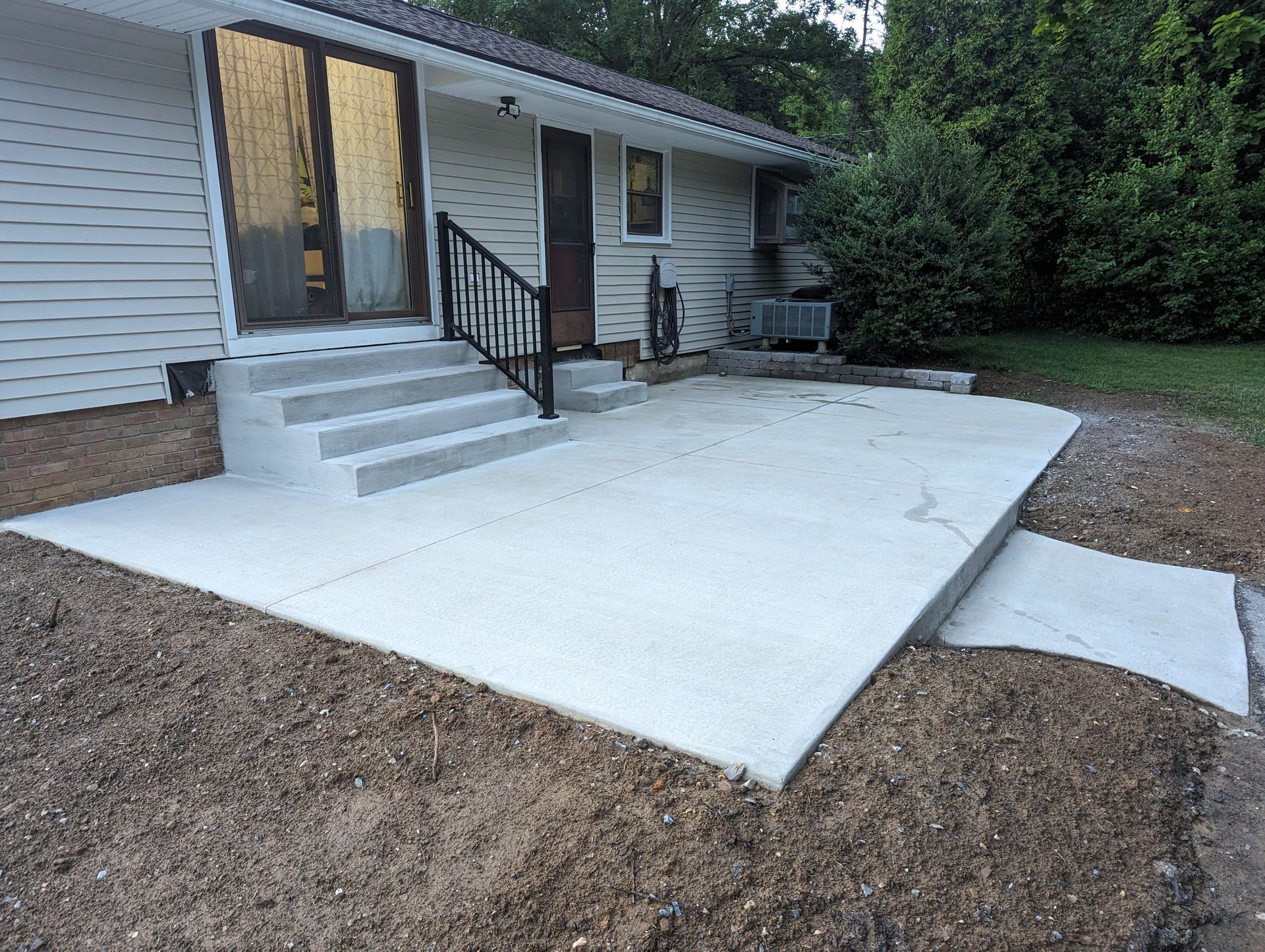 Exterior view of a house with concrete patio, steps, and handrail.