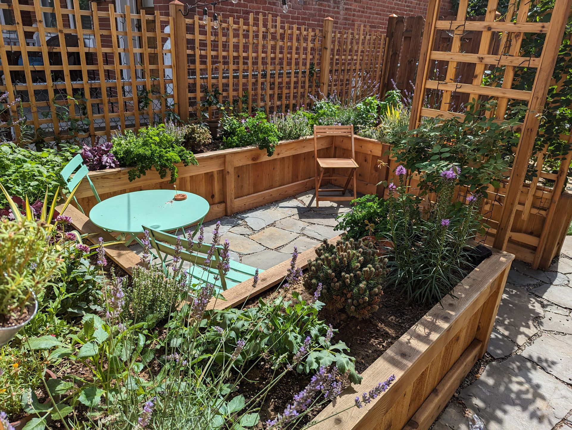 A small urban garden with wooden planters, a patio, and light teal outdoor furniture.