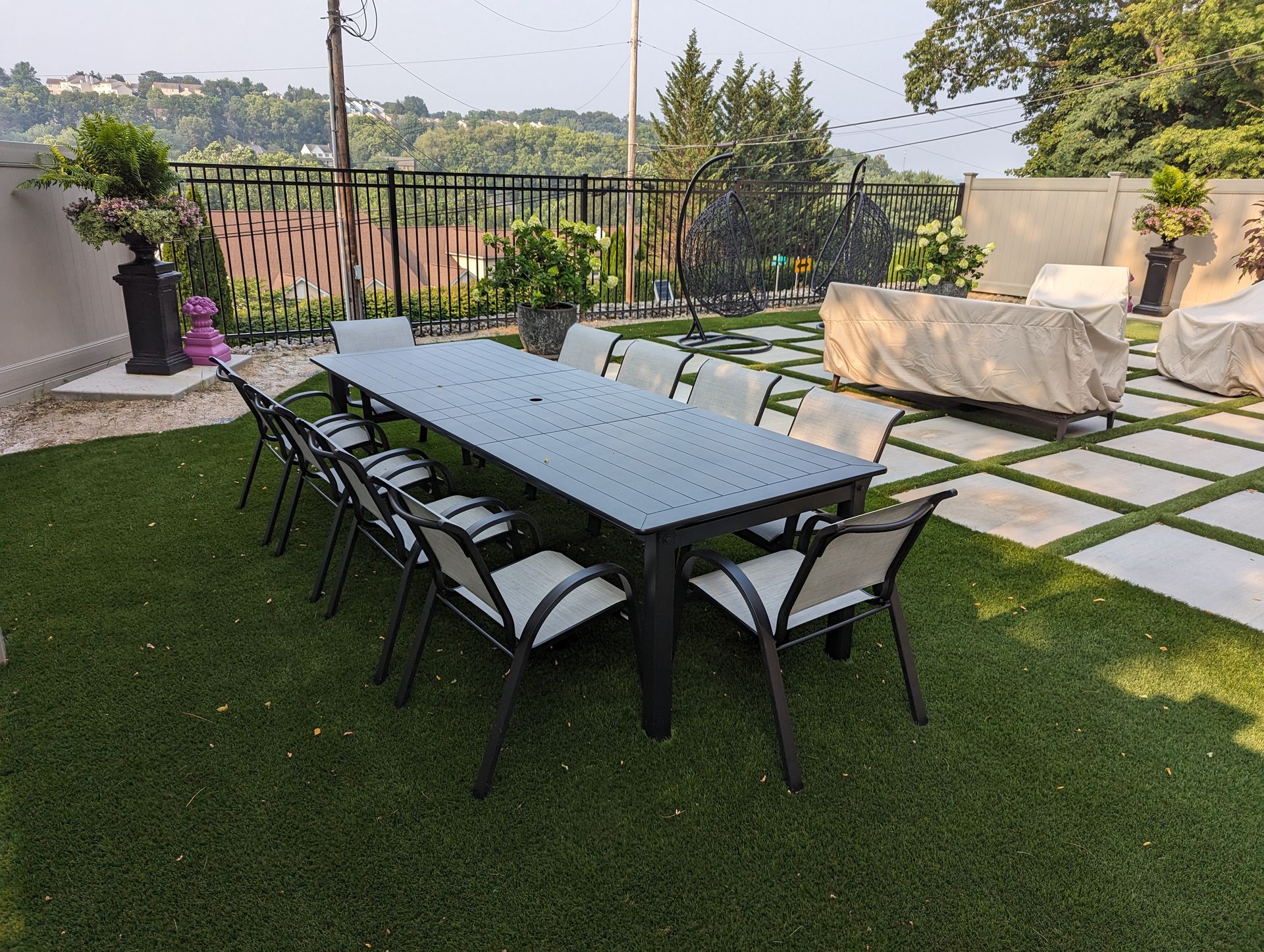 Outdoor dining table with chairs on a green lawn with stone pavers, overlooking a distant landscape.