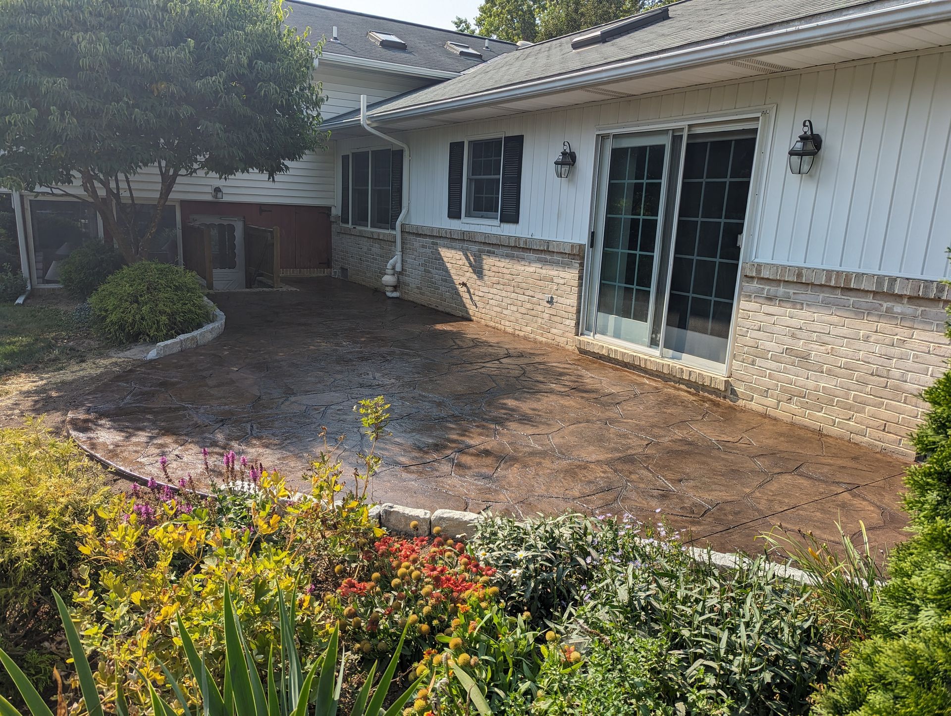 Backyard patio with brown brick facade, sliding glass doors, and surrounding greenery.