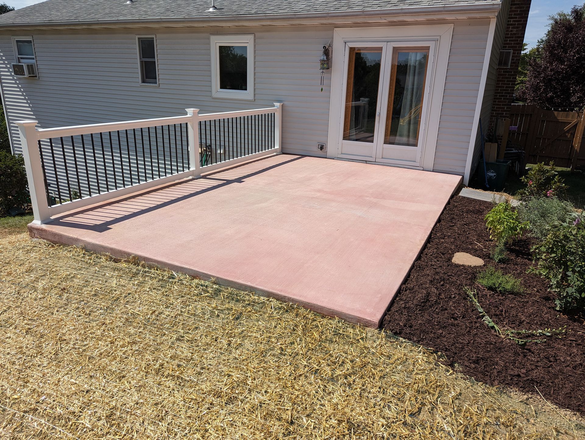 Red concrete patio with railing, next to a house with French doors and dried grass.