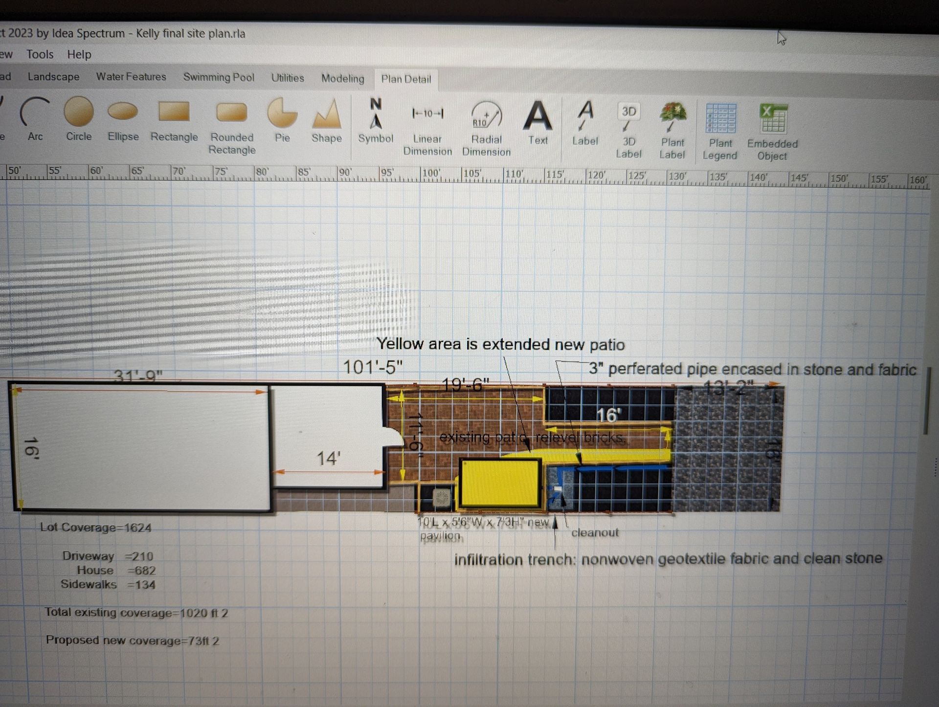 Landscaped rock garden with green plants, rocks, and small trees next to a parking area with blue vehicles.