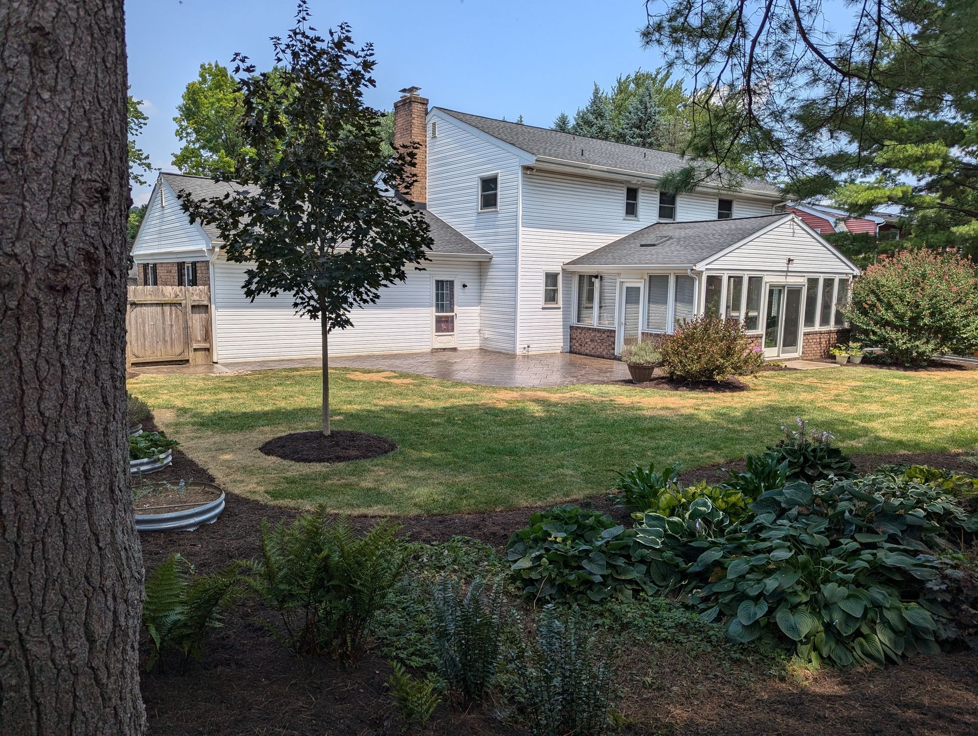 Backyard of a two-story white house with a screened porch and landscaped yard.