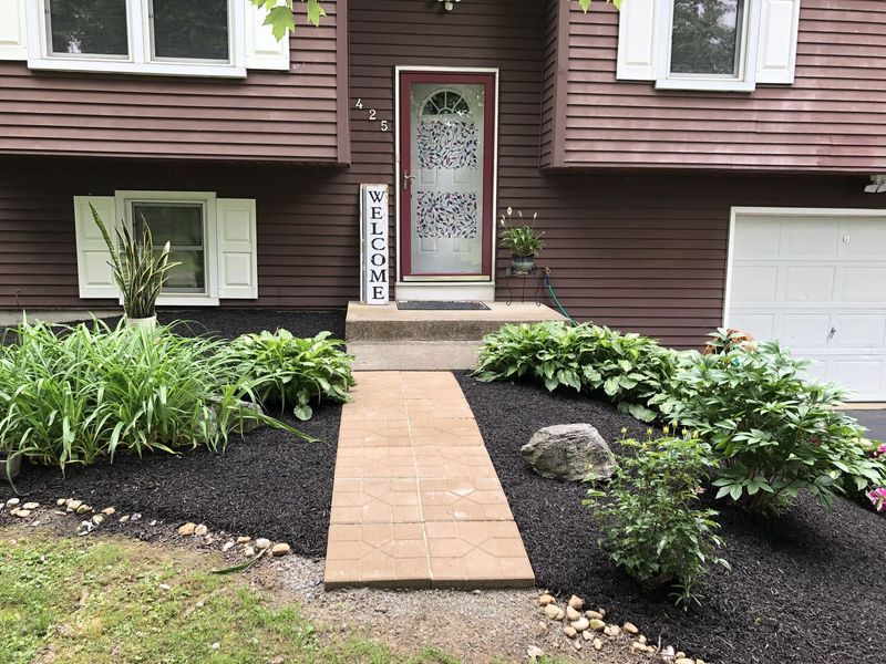 Brown house with a paved walkway, black mulch, and landscaping.
