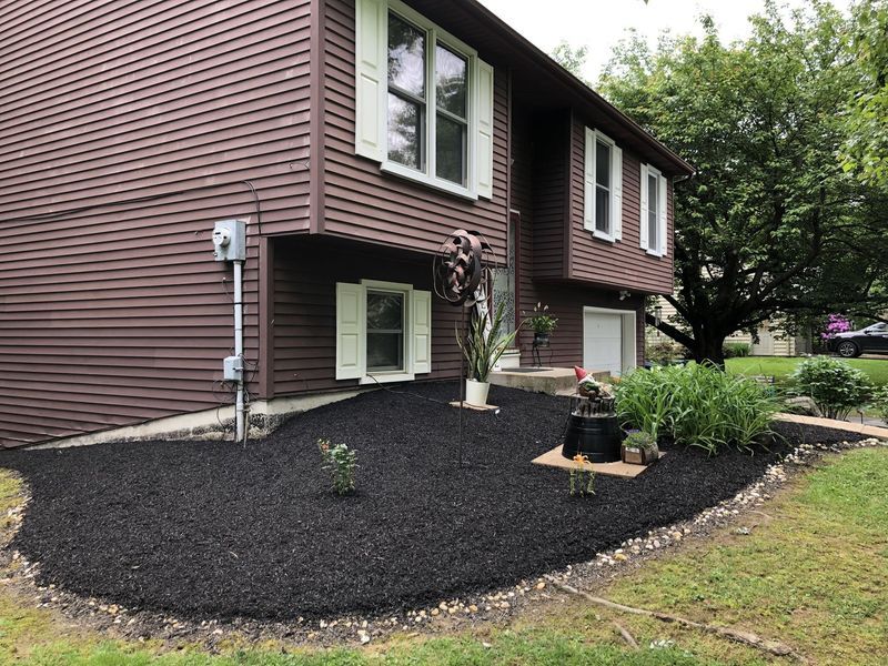 Brown house with black mulch landscaping, green grass, and small plants.