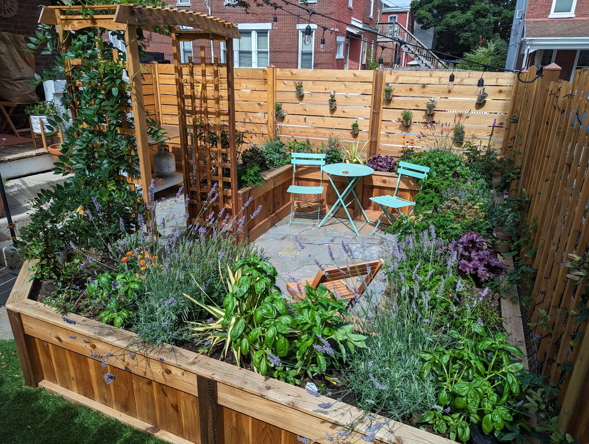 A small garden with raised beds, wooden structures, a small table and chairs, and various plants.