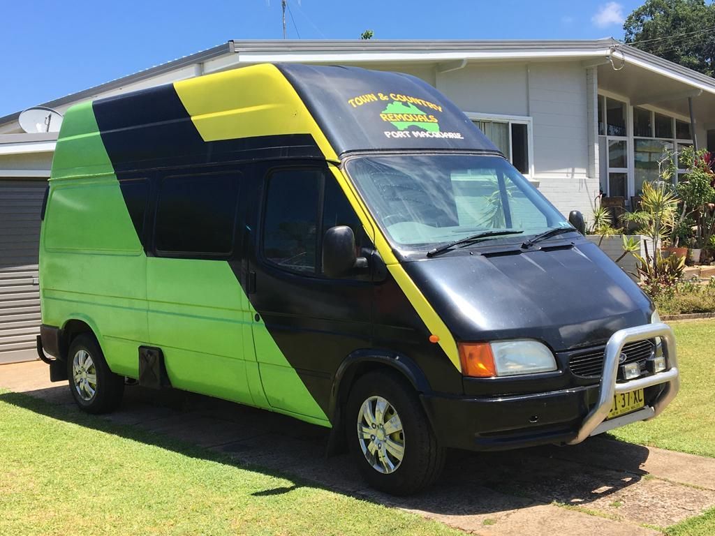 A Black Moving Van Parked in Front of a Residential House — Town & Country Removals In Port Macquarie, NSW