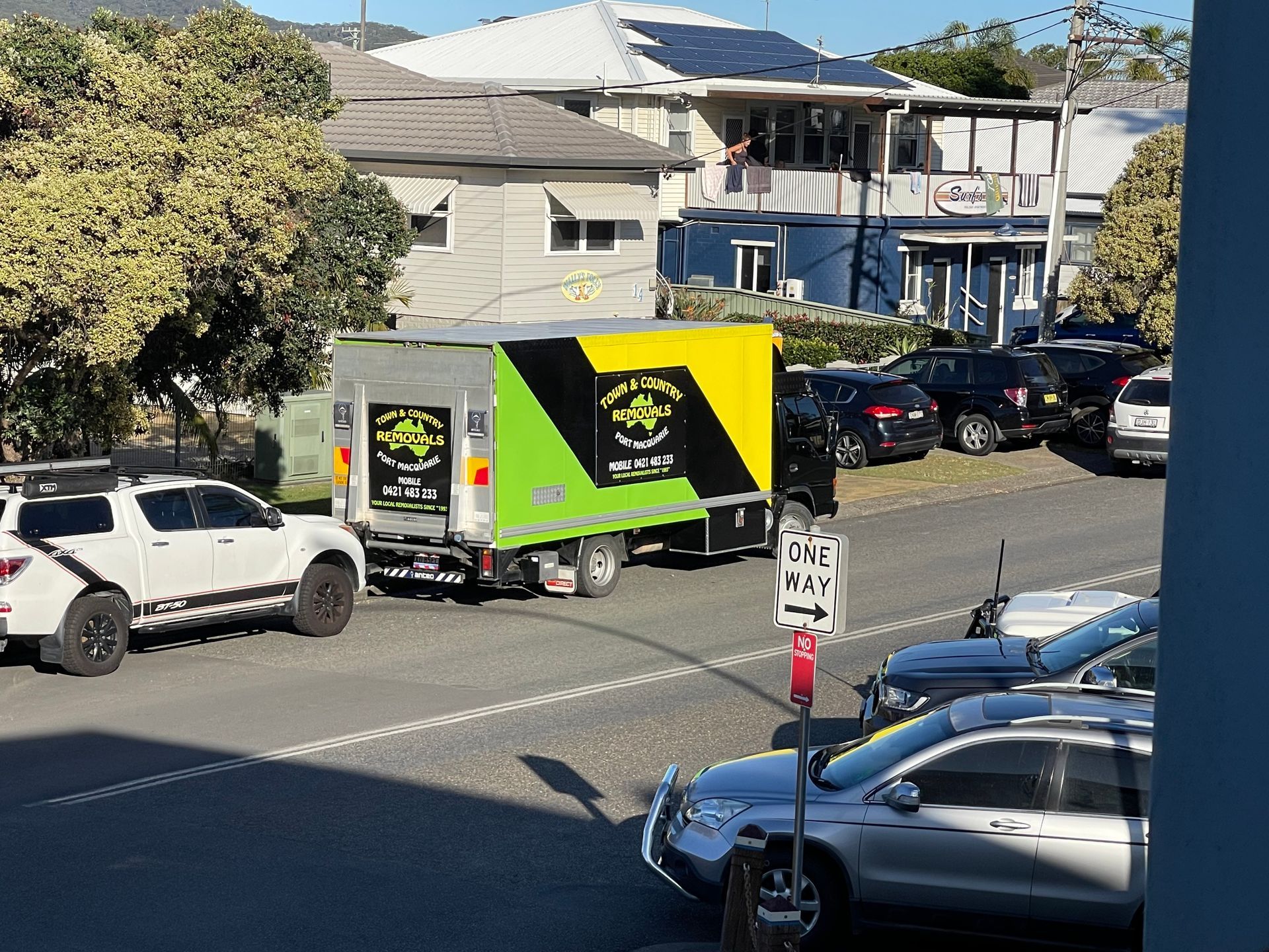 A Green and Yellow and Black Moving Truck Parked on a Busy Street  — Town & Country Removals In Port Macquarie, NSW
