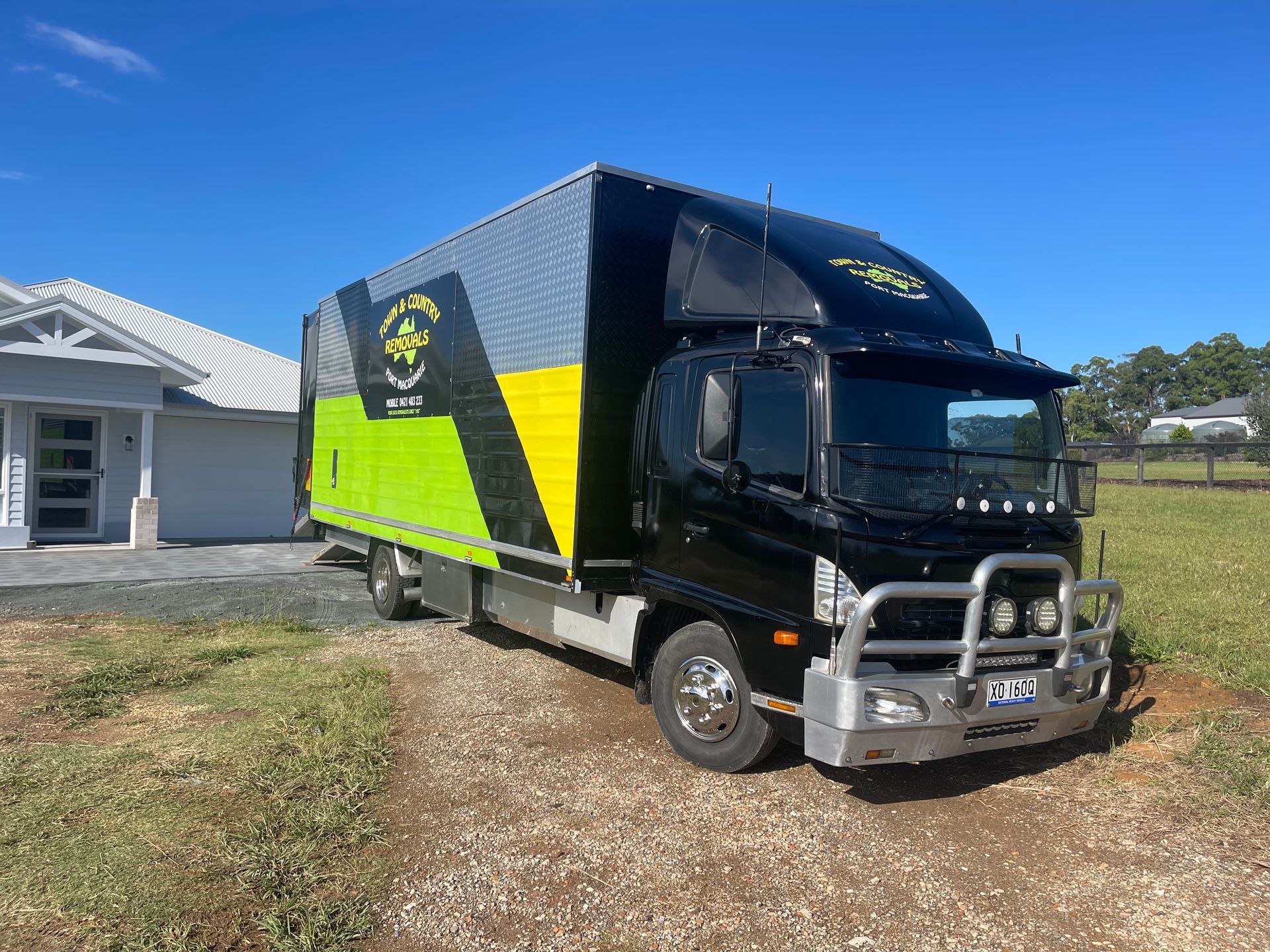 A Green Moving Truck Parked in Front of a House — Town & Country Removals In Port Macquarie, NSW