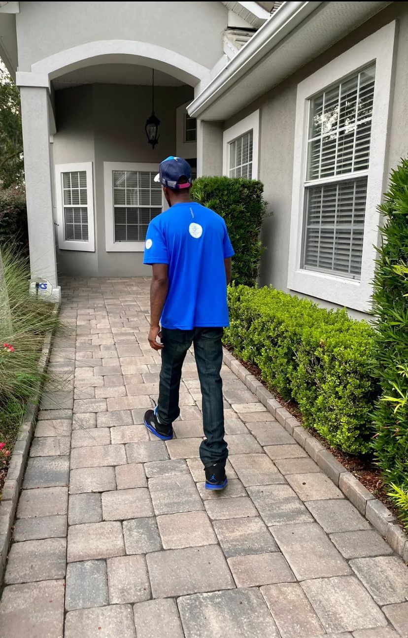 A man in a blue shirt is walking down a brick walkway towards a house.