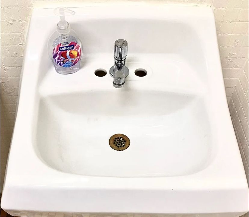 A white bathroom sink with a bottle of hand soap on top of it. BEFORE/AFTER