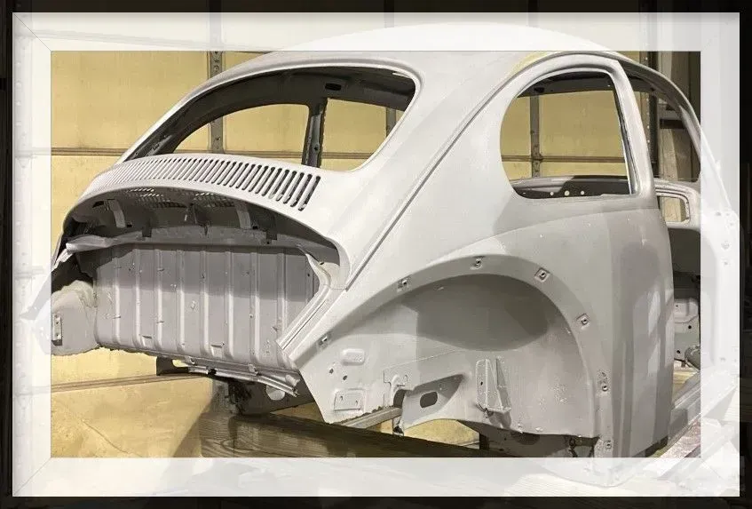 Gray, primer-coated vintage Volkswagen Beetle body shell; workshop setting.