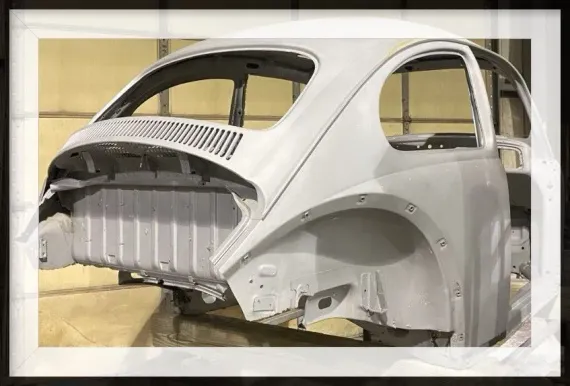 Gray, primer-coated vintage Volkswagen Beetle body shell; workshop setting.