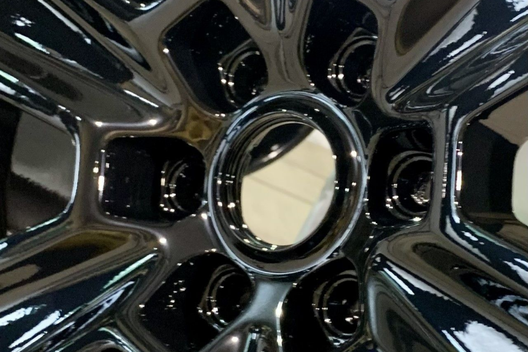 Close-up of a shiny, black car wheel with a central opening, reflecting the surrounding environment.