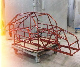 Red race car frame on a rolling cart, in an industrial setting.