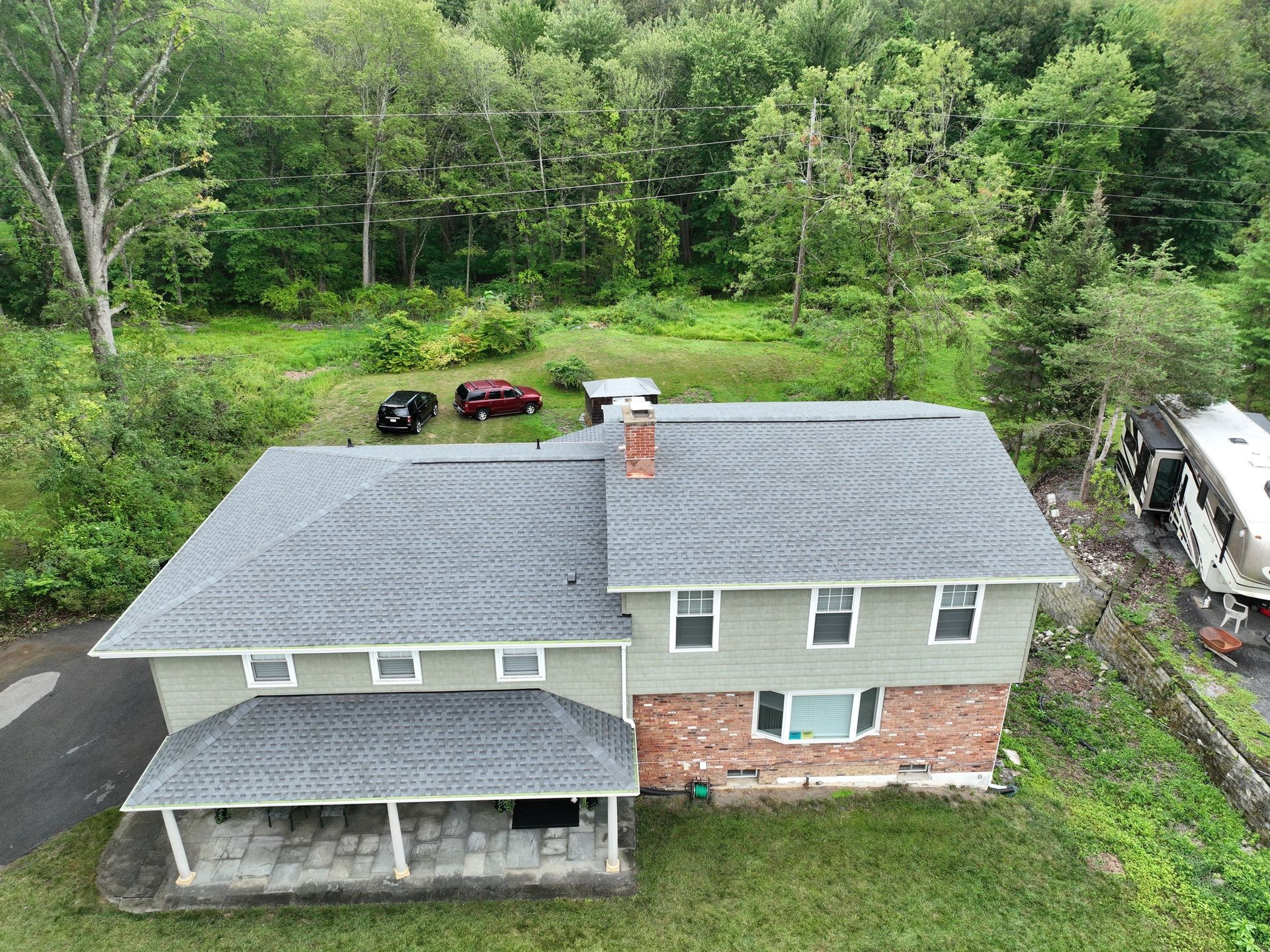 An aerial view of a green house with a gray asphalt roof replacement