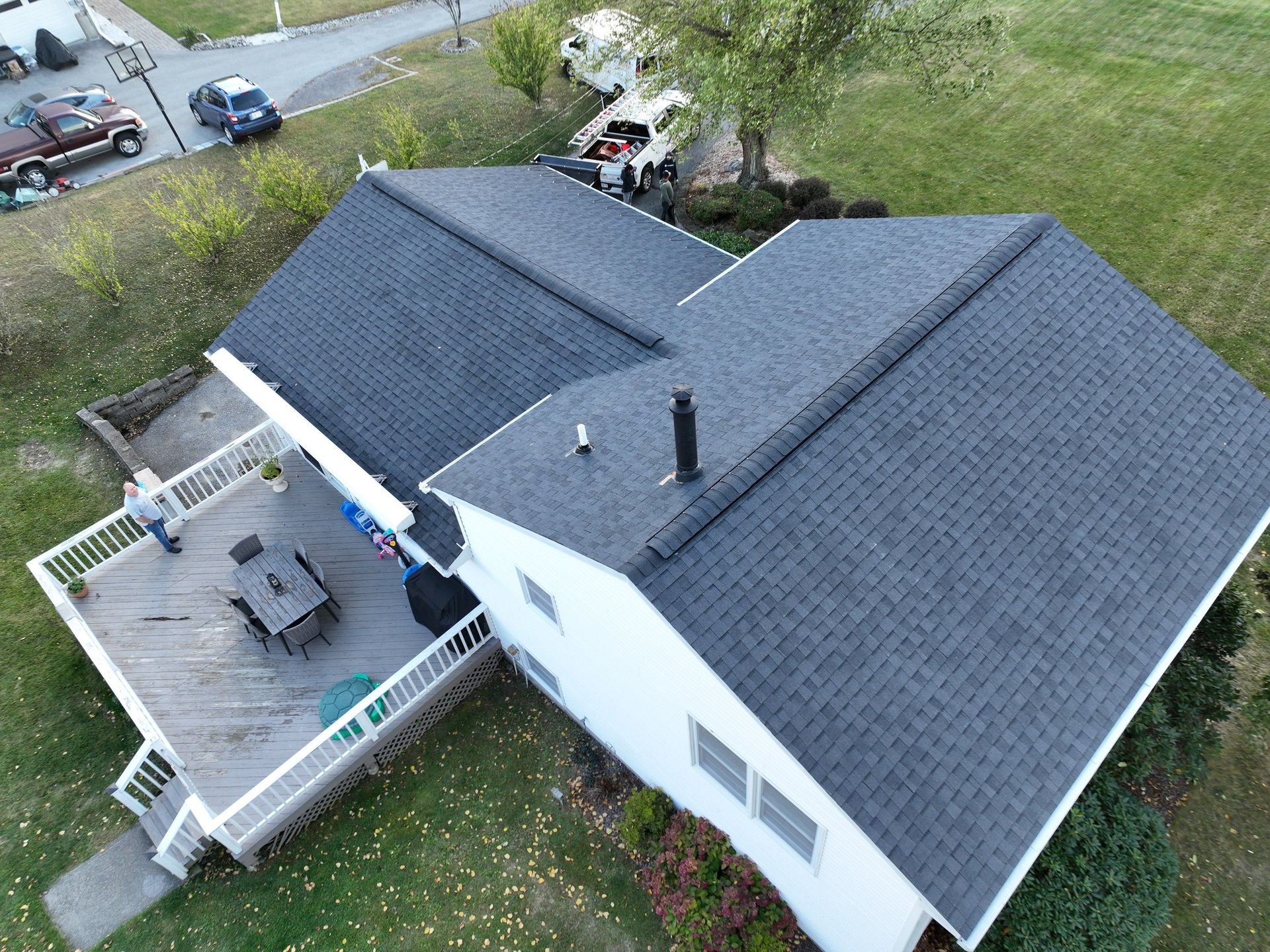 An aerial view of a white house with a black roof replacement and a new deck.