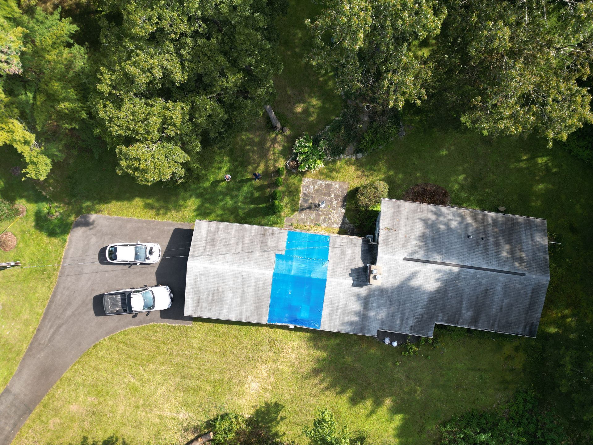 An aerial view of a house with a tarp on the roof being repaired with emergency roofing services