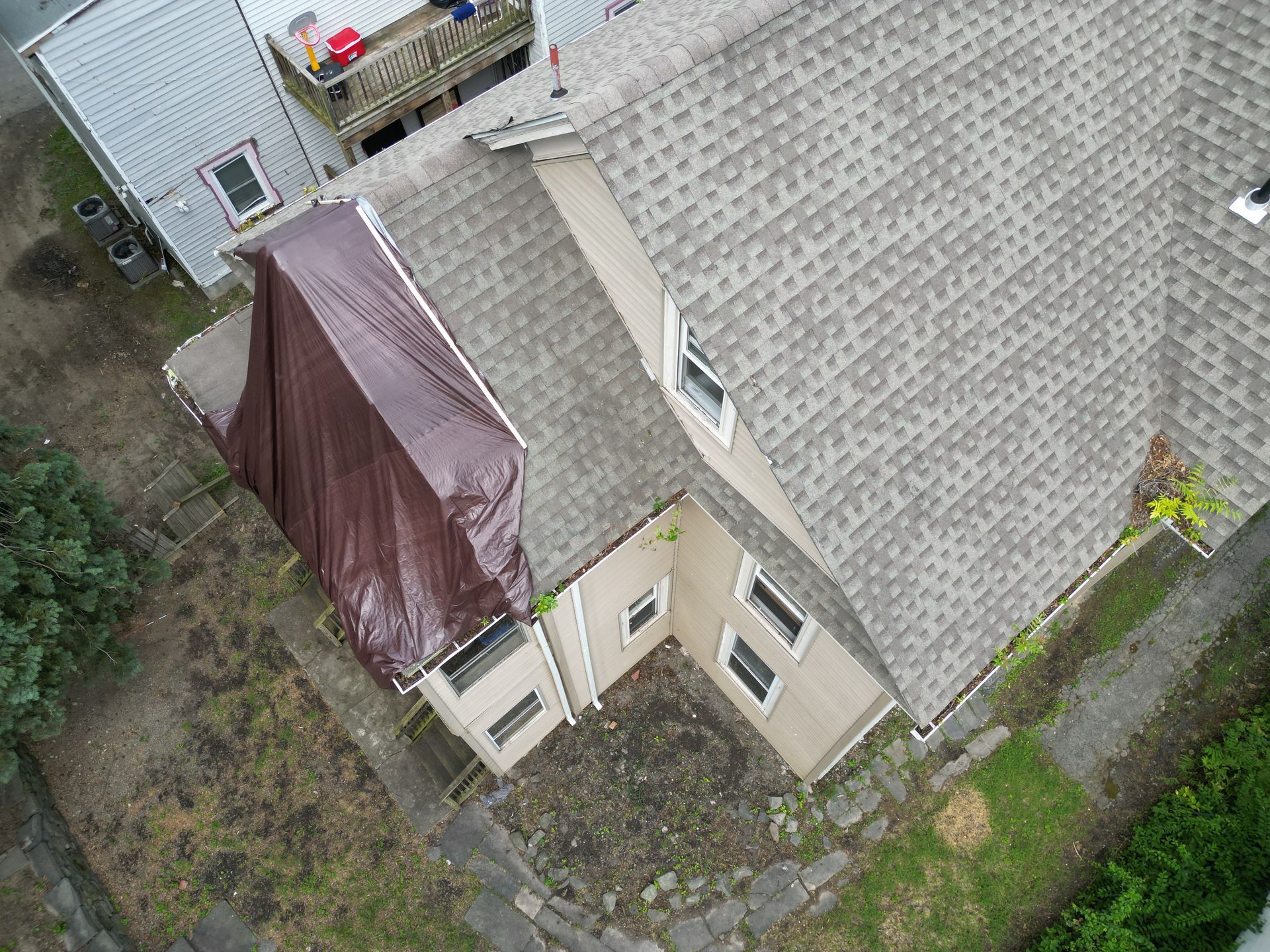 An aerial view of a house with a tarp on the roof being repaired from storm damage
