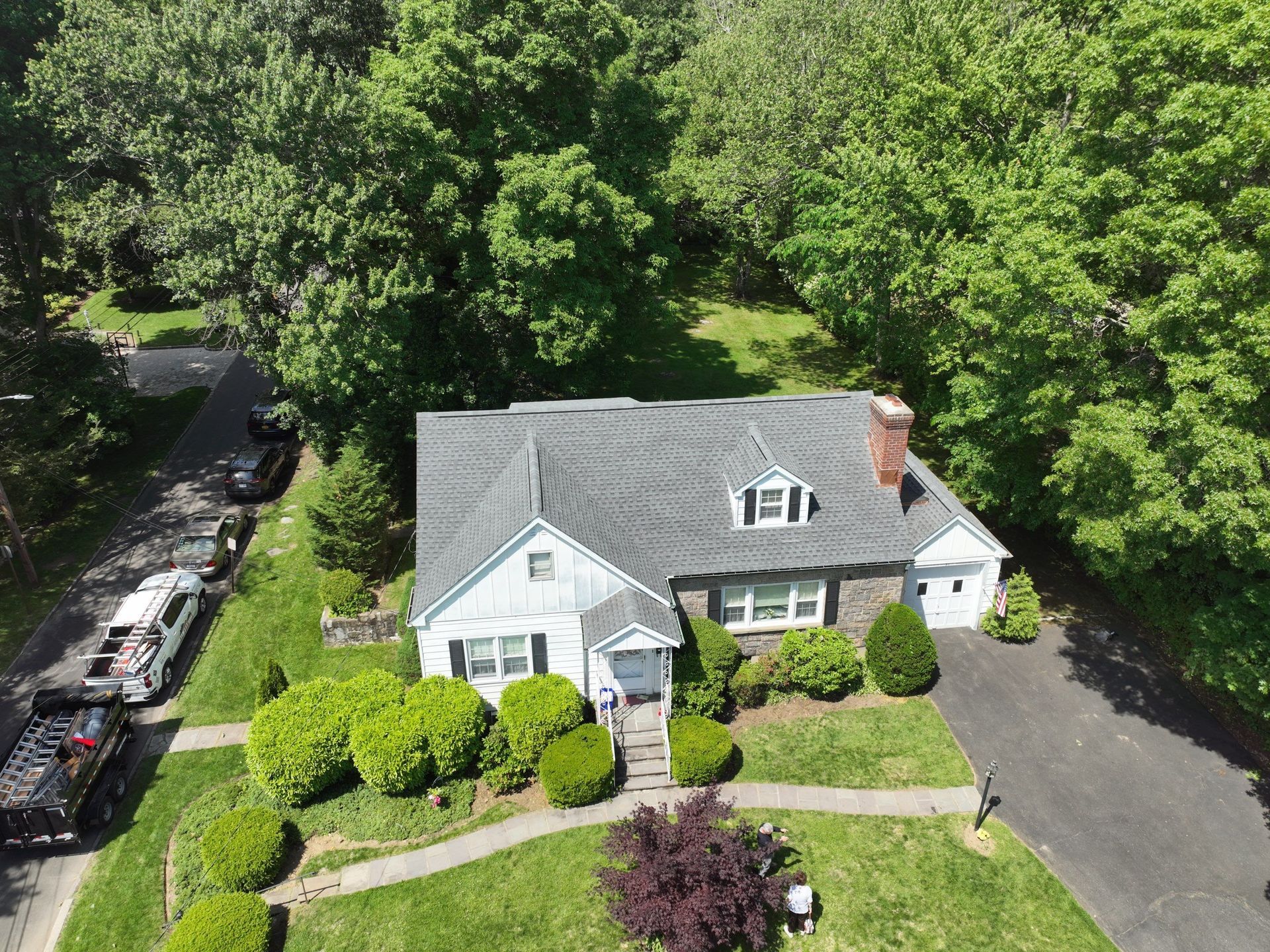 An aerial view of front of a white house with a gray asphalt roof replacement 