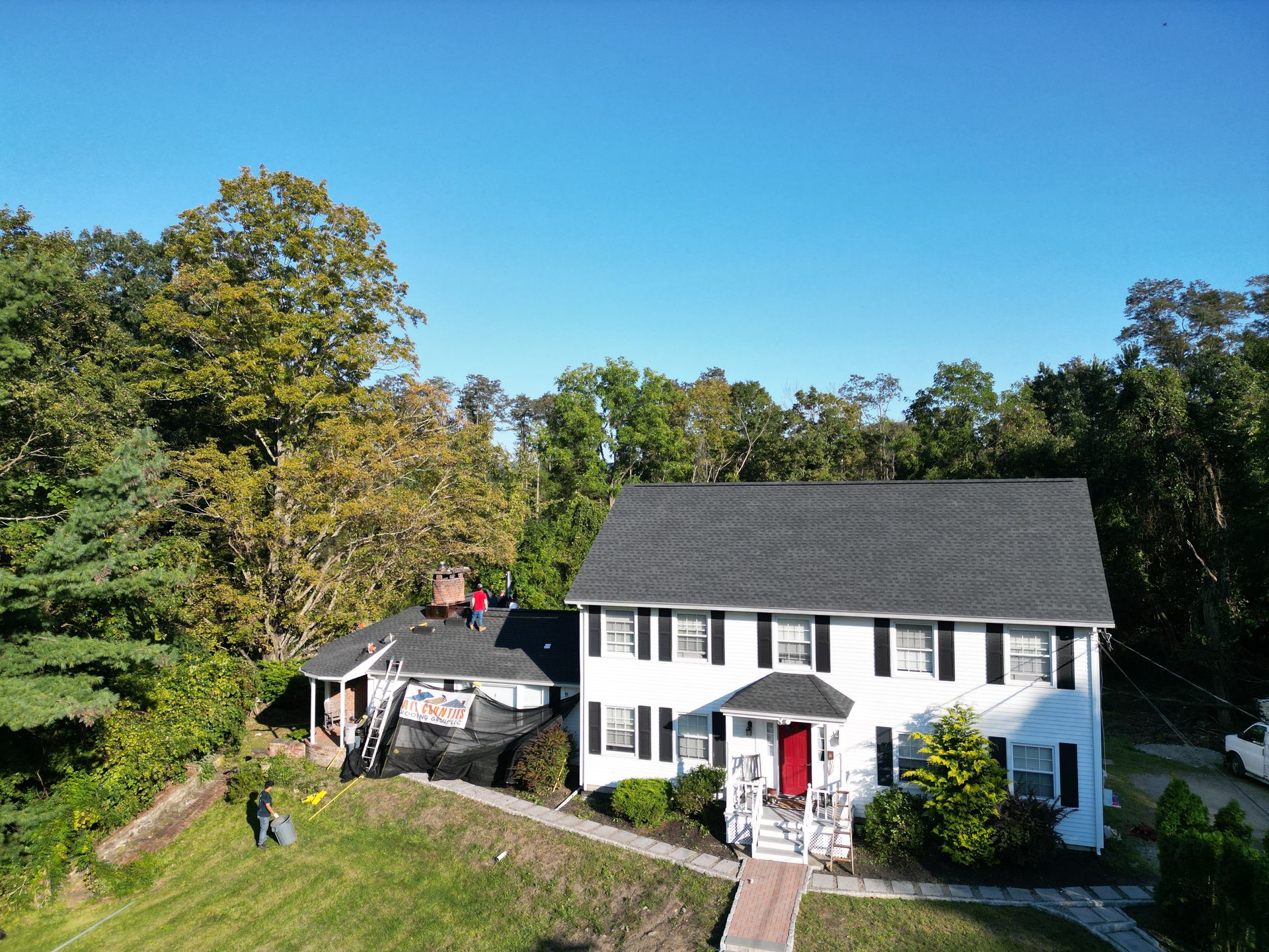 An aerial view of a large white house that received a dark roof replacement