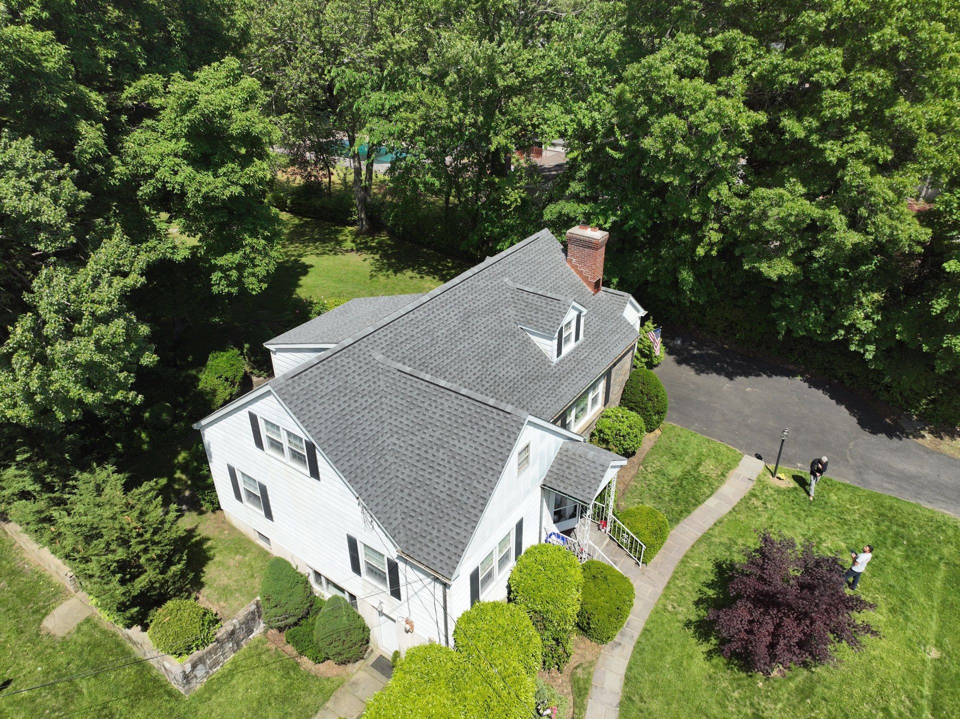 A side aerial view of a large white house with asphalt roof replacement