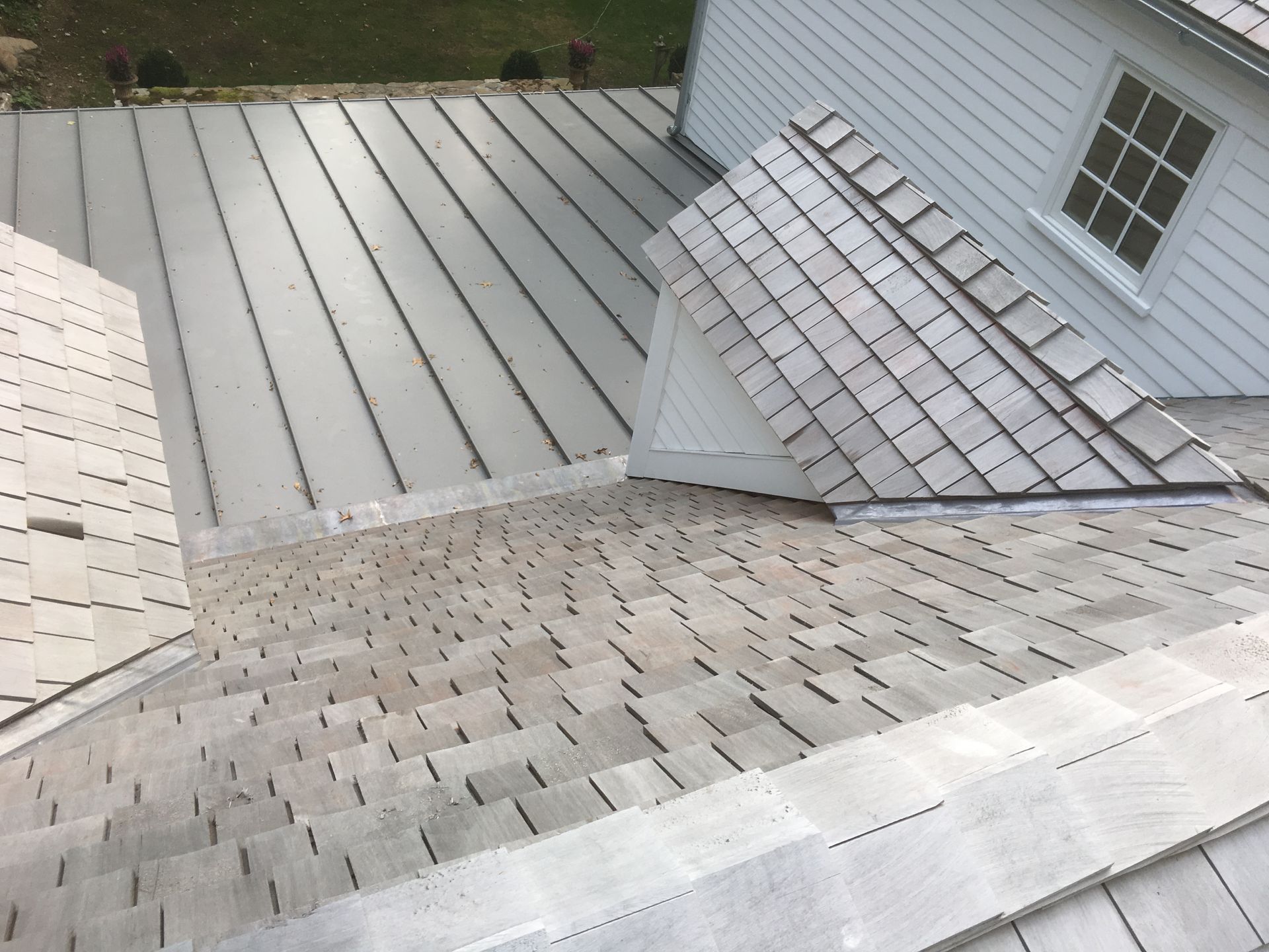 A white house with a metal roof and a yellow cedar roof