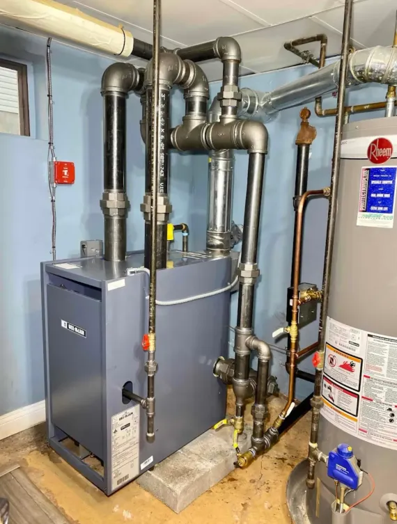 Boiler room with gray HVAC units, exposed pipes, and a water heater on a concrete floor