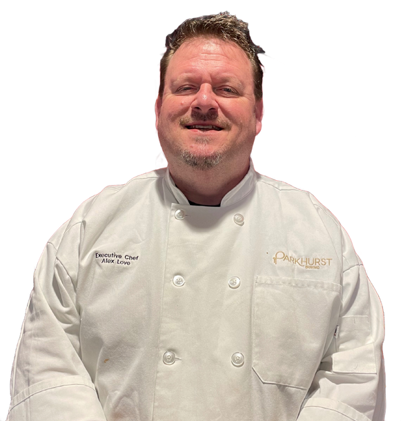 A chef in a white uniform with a Parkhurst logo smiling.