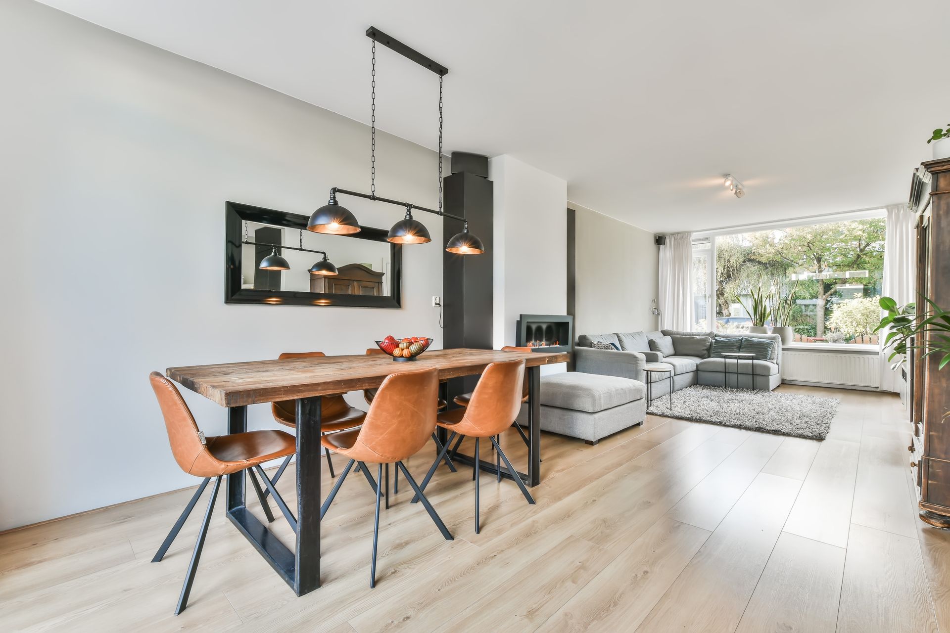 Dining area with wooden table, orange chairs, and black pendant lights.  Living room with sofa and window.
