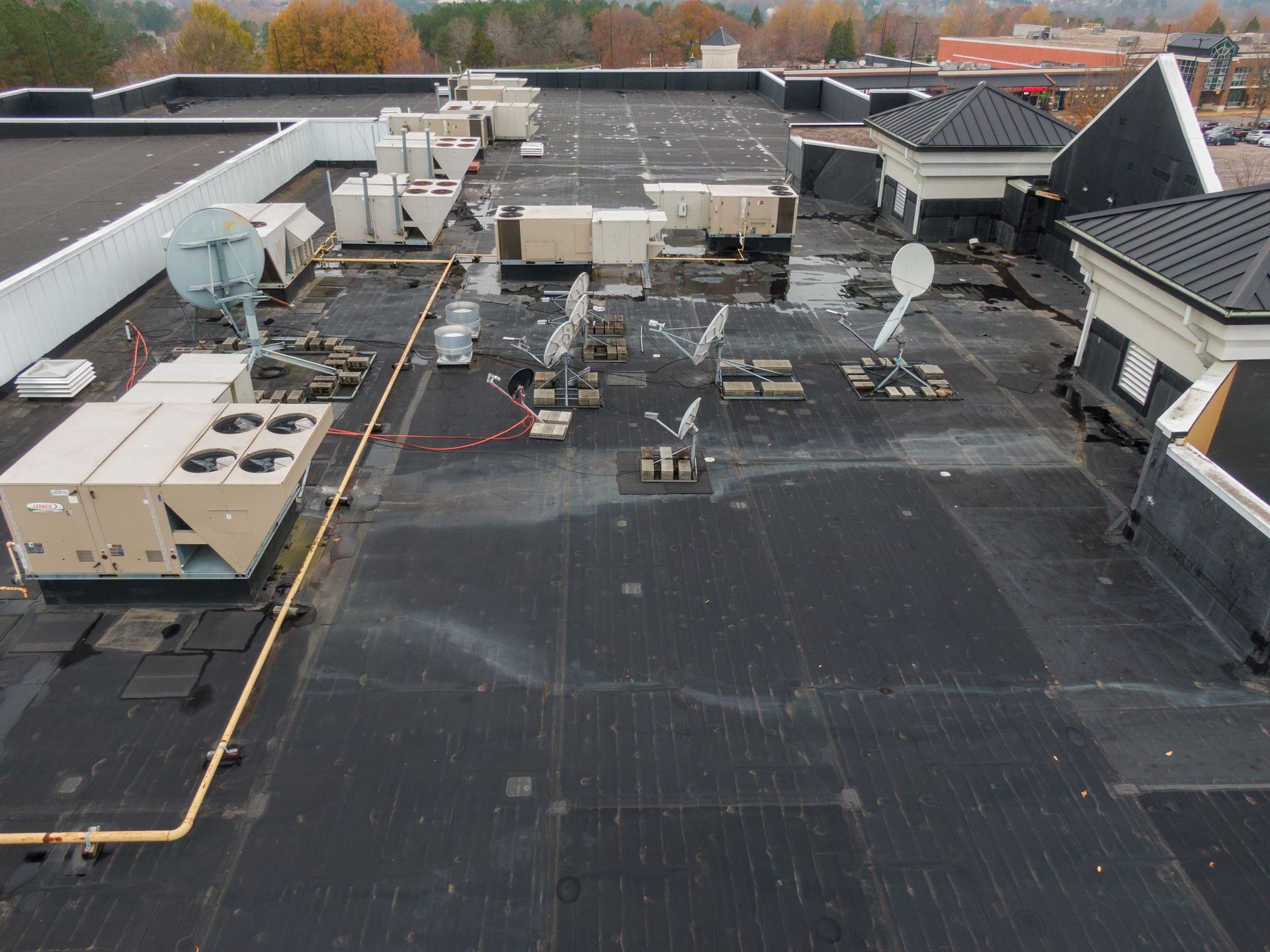 Rooftop with HVAC units, satellite dishes, and pipes on a flat black roof under overcast skies