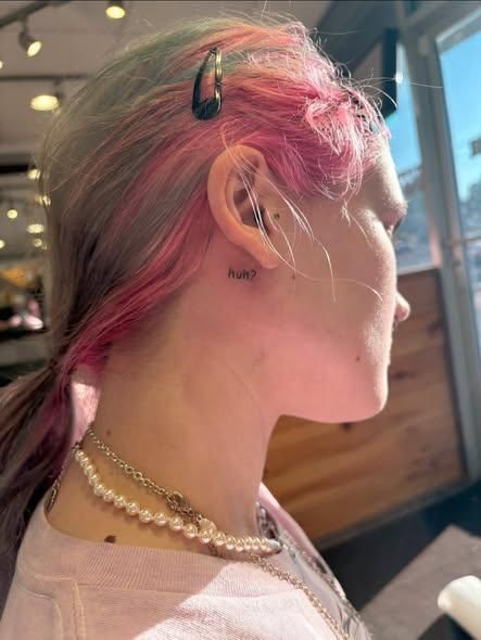 Person with colorful hair, side profile. Tattoo near ear, pearl necklace.