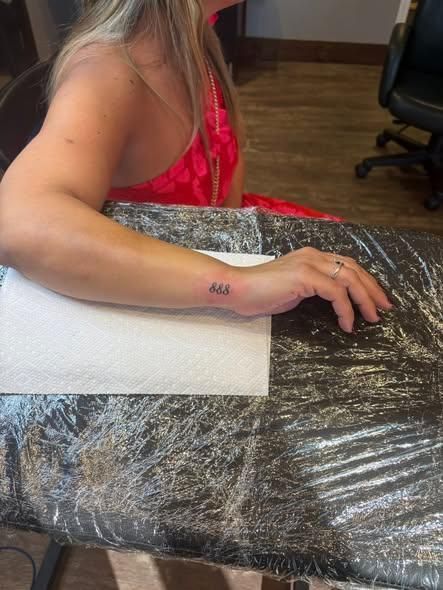 Arm with small tattoo on wrist resting on covered table.