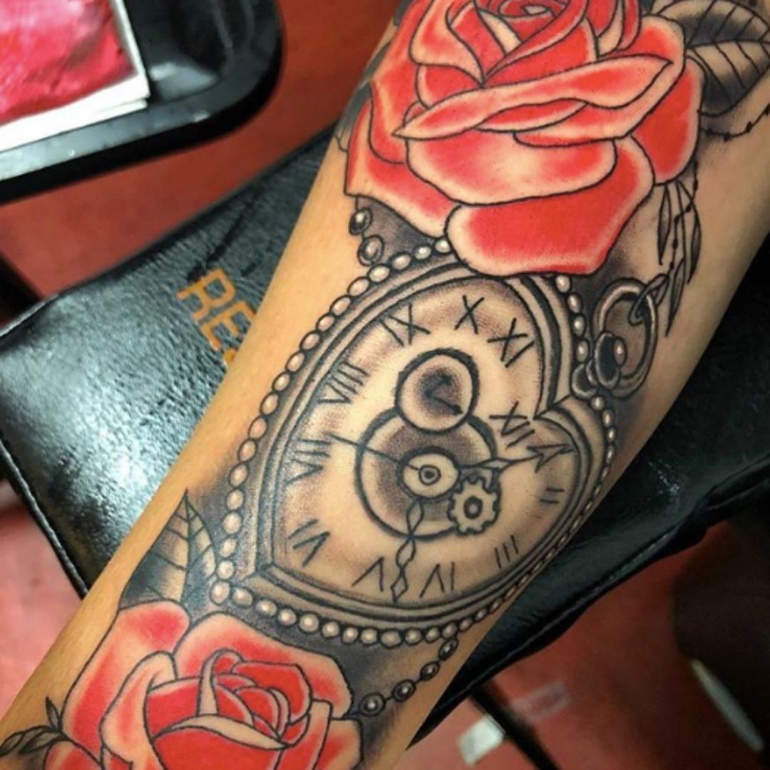 Tattoo of red roses and a heart-shaped pocket watch with Roman numerals on an arm.