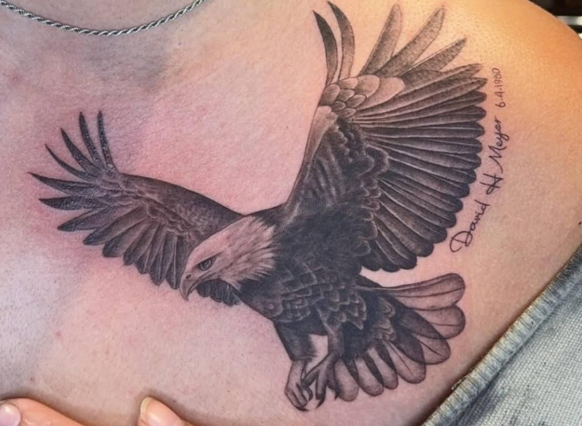 Tattoo of a bald eagle in flight, detailed black and white shading, on a person's shoulder.