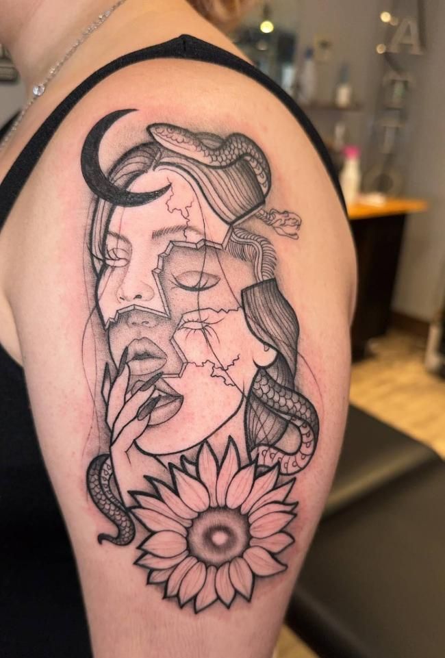 Black and gray tattoo on shoulder: faces with a crescent moon, snake, sunflower, and broken lines.