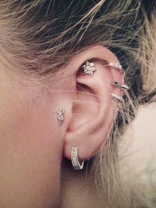 Ear with multiple silver earrings, including hoops, studs, and helix piercings.