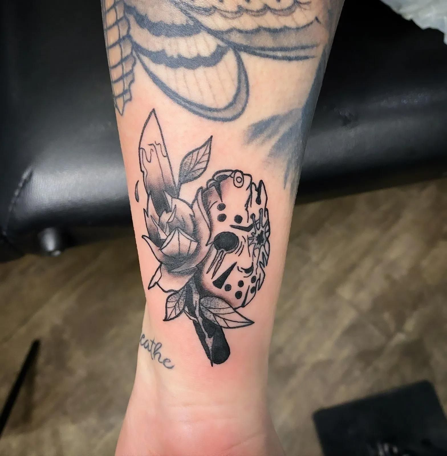 Tattoo on forearm: Jason Voorhees hockey mask with a rose, black and gray ink.
