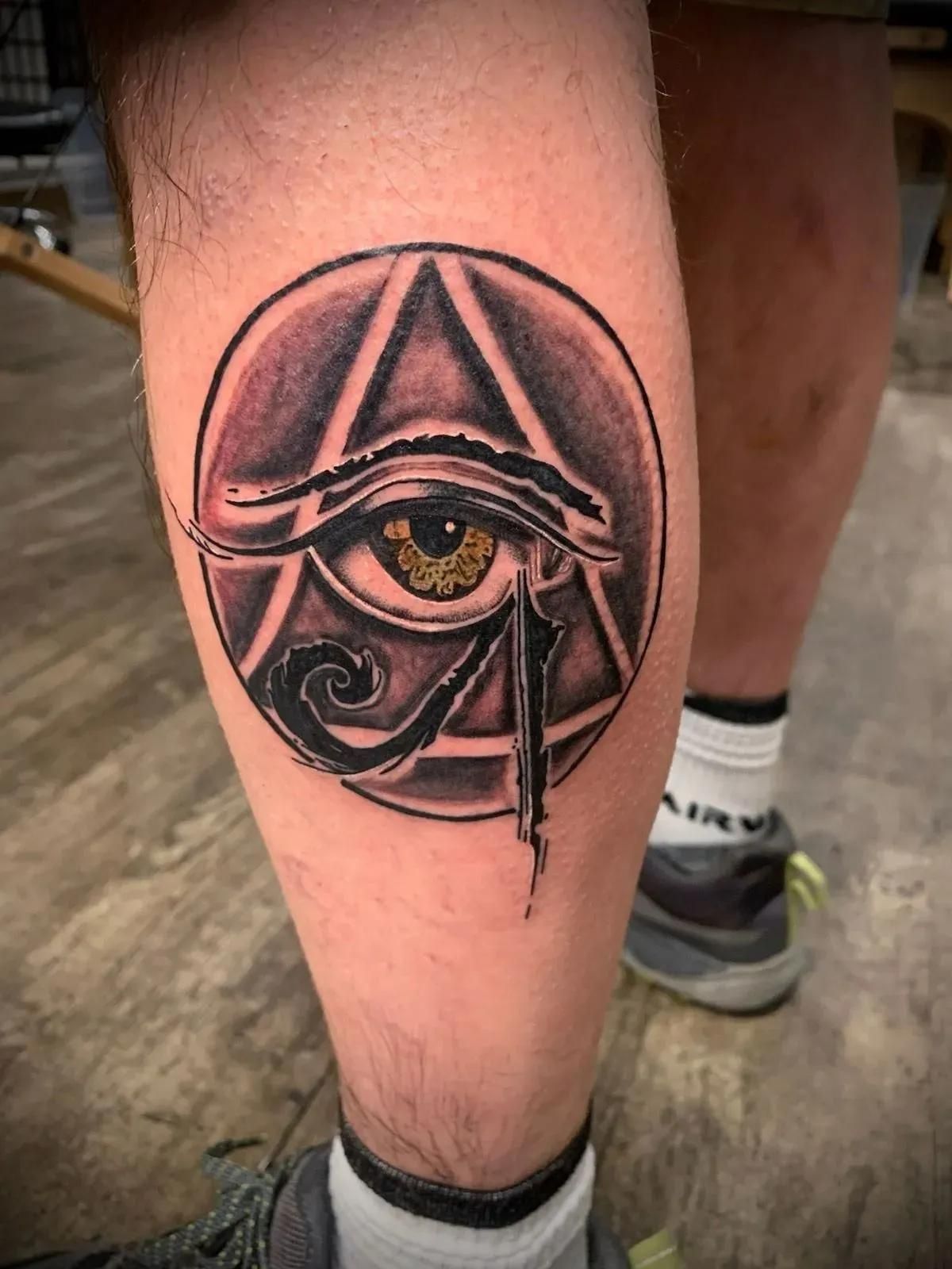 Tattoo of the Eye of Horus within a triangle and circle on a calf. 