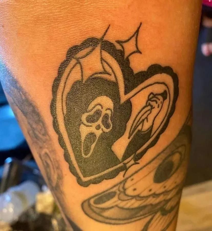 Tattoo of Ghostface mask and knife inside a heart, on arm.