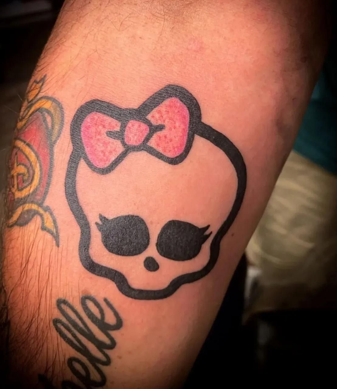 Tattoo of a skull with a pink bow on an arm. 