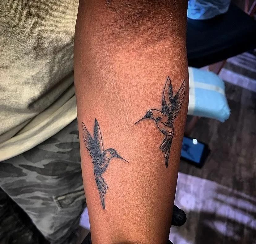 Two hummingbird tattoos on a person's arm, gray ink. 